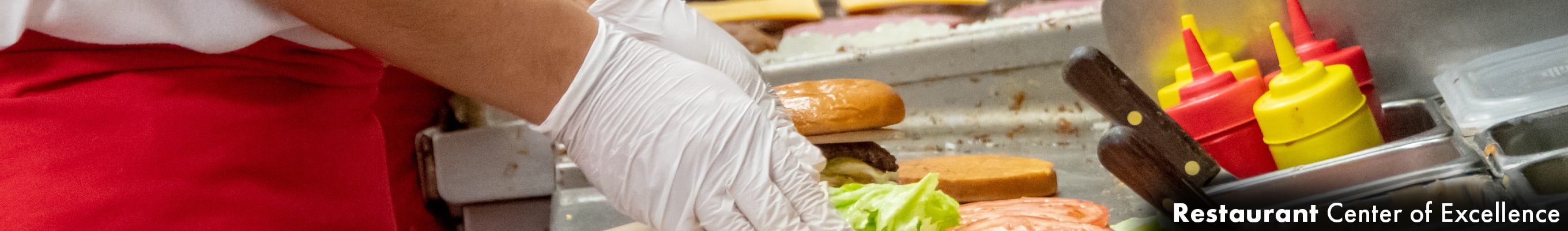 gloved hands preparing a hamburger, placing on toppings and placing the bun on top before serving