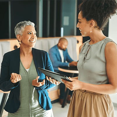 Expert Advice an elderly woman with short gray hair in business atire seems to be offering advice or explaining something to a younger woman who has a clipboard or tablet to take notes