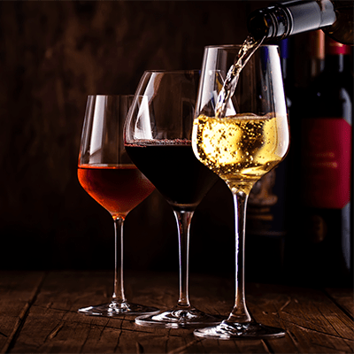 three wine glasses staggered side-by-side, one filled with rose, another with red wine, another with white, still being poured
