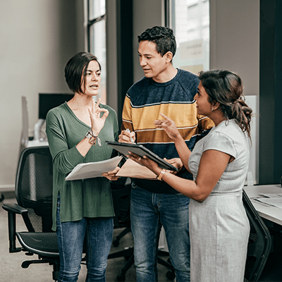 a couple being guided by an older professional woman, who is showing them something on a tablet
