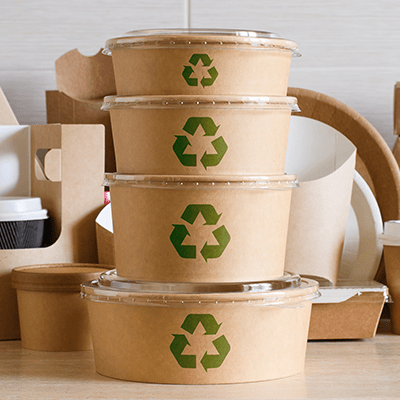 a stack of paper containers with the green recycling symbol on their exterior. Other sustainable products on display in the background