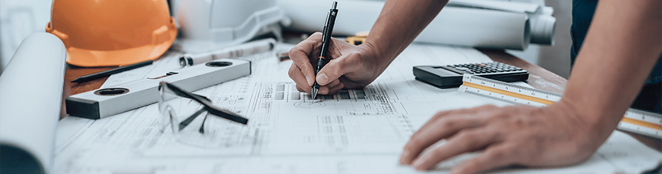 a project manager pouring over the blueprints of a project, surrounded by measuring tools, and construction hat and eye-cover glasses on the table