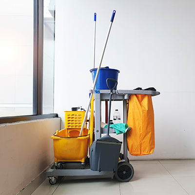 Janitorial cart equipped with cleaning supplies and tools in an office corridor.