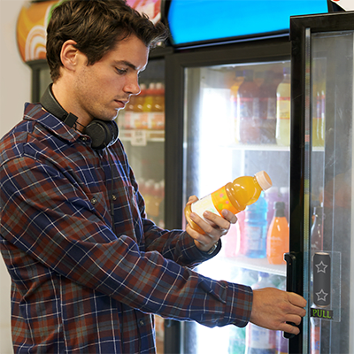Man examining a bottle of juice in front of an open beverage cooler in a micro-market.