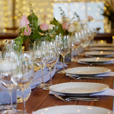 a long row of neatly arrange plates, silverware, wine glasses, well lit room, flowers in the background
