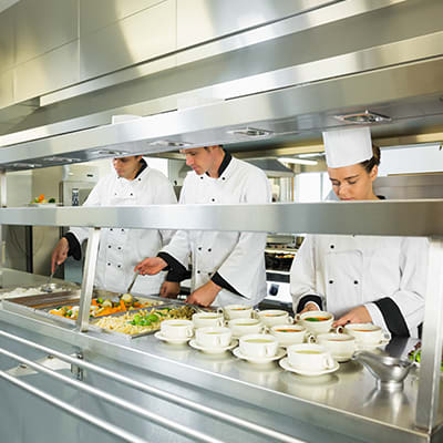 Chefs preparing food in a commercial kitchen with stainless steel foodservice equipment and supplies.