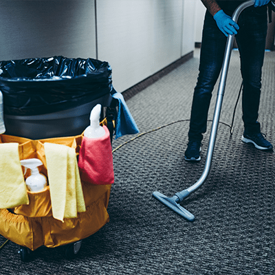 Janitorial staff cleaning a carpeted floor with a vacuum cleaner, representing maintenance and janitorial solutions in a professional setting