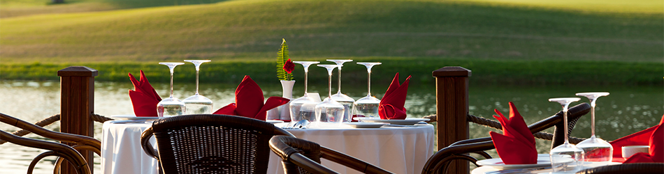 An elegant outdoor dining setup overlooking a serene lake, featuring a table with fine glassware and folded red napkins, ready for a high-end golf, social, or country club event.