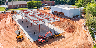 Design & Build An aerial view of a construction site with the structural framework of a building in progress, heavy machinery, and dirt grounds.